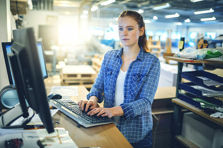 Warehouse employee using a desktop computer to manage logistics operations in a fulfillment center.