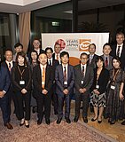A group of Japanese Gebrüder Weiss employees stand in front of a sign showing 25 years in Japan